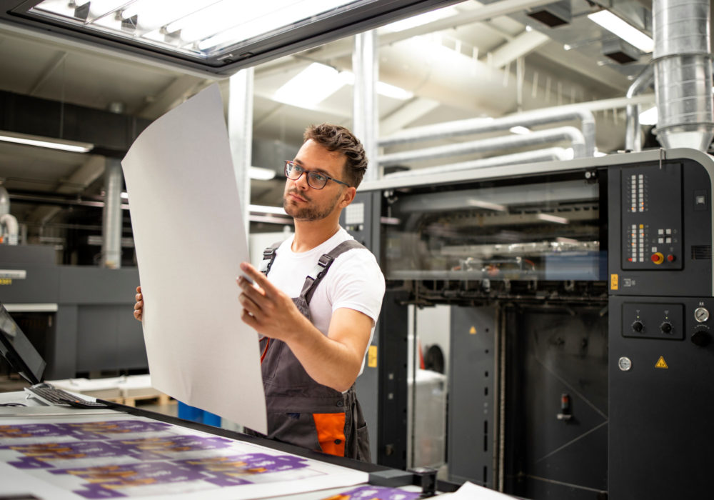Print shop worker checking quality of imprint and controlling printing process.