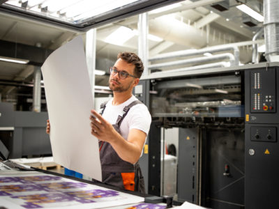Print shop worker checking quality of imprint and controlling printing process.
